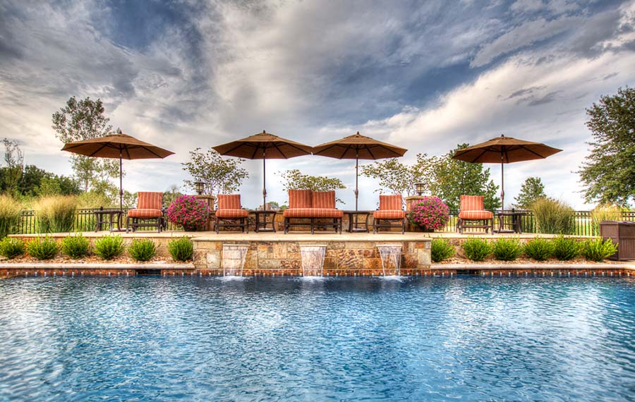 A pool with entertainment centers, outdoor kitchens, fountains, and waterfalls built by Backyard by Design Kansas City