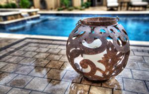 Image of iron votive on a beautiful tile table in front of a Backyard by Design Pool