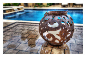 Image of iron votive on a beautiful tile table in front of a Backyard by Design Pool